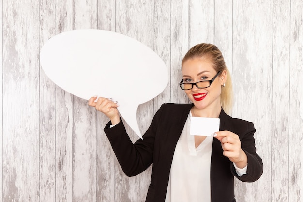 Photo gratuite vue de face jeune femme d'affaires dans des vêtements stricts veste noire tenant énorme signe blanc et carte sur surface blanche