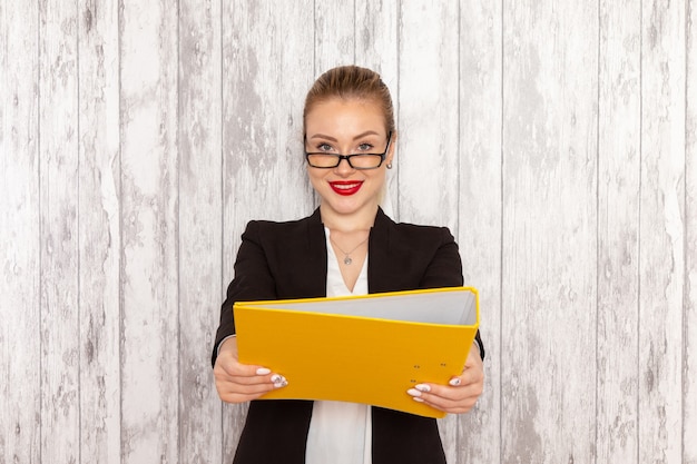 Vue de face jeune femme d'affaires dans des vêtements stricts veste noire tenant des fichiers et des documents sur un bureau blanc clair