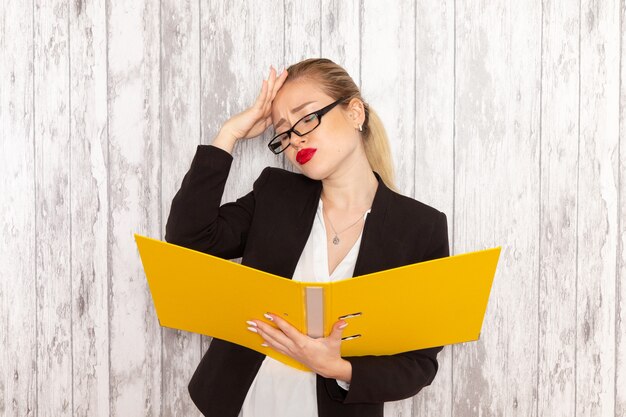 Vue de face jeune femme d'affaires dans des vêtements stricts veste noire tenant des fichiers et des documents sur la surface blanc clair