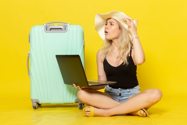 Vue de face jeune femme à l'aide d'un ordinateur portable sur le bureau jaune fille voyage voyage vacances voyage soleil