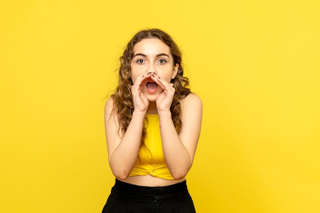 Vue de face de la jeune femme appelant quelqu'un sur le mur jaune