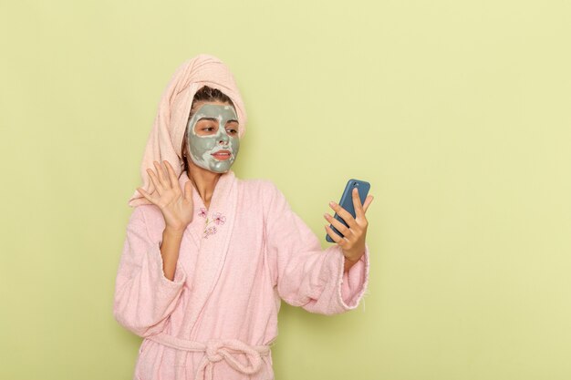 Vue de face jeune femme après la douche en peignoir rose à l'aide de son téléphone sur une surface verte