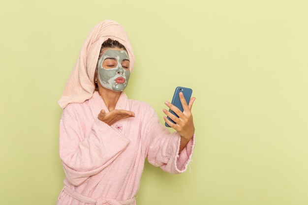 Vue de face jeune femme après la douche en peignoir rose à l'aide de son téléphone sur une surface verte