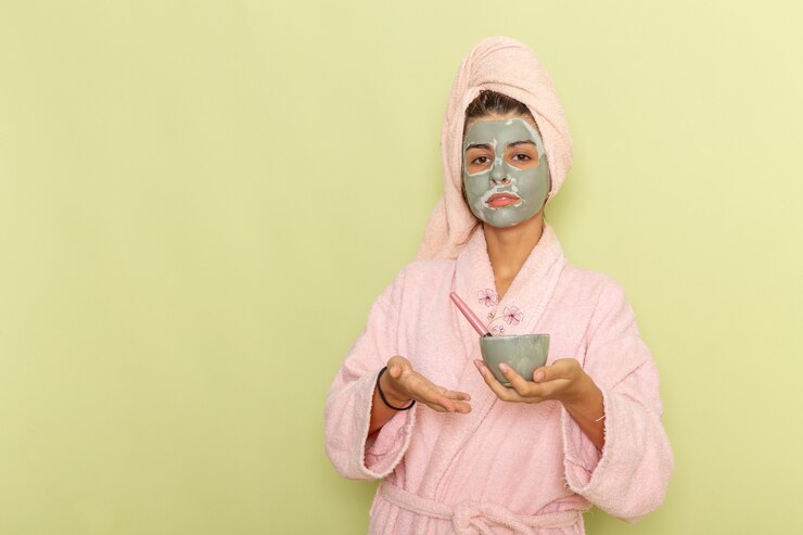 Photo gratuit vue de face jeune femme après la douche en peignoir rose appliquant un masque sur une surface verte