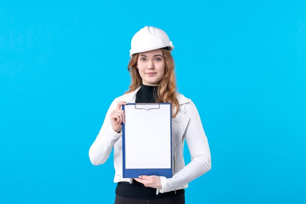 Vue de face jeune femme architecte en casque sur bleu