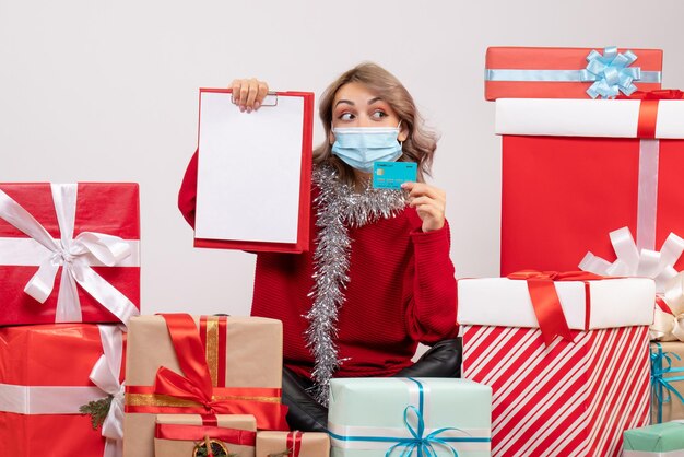 Vue de face jeune femme assise autour de cadeaux avec carte bancaire