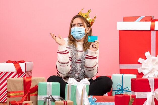 Vue de face jeune femme assise autour de cadeaux de Noël avec carte bancaire