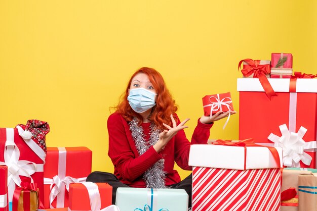 Vue de face jeune femme assise autour de cadeaux de Noël en masque sur jaune