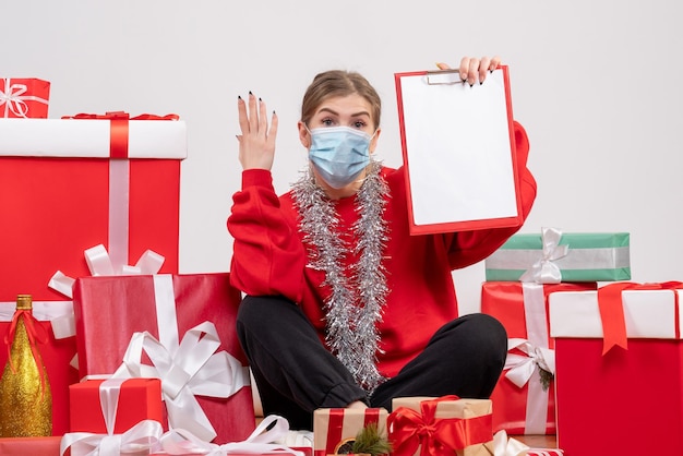 Vue de face jeune femme assise autour de cadeaux de Noël en masque stérile