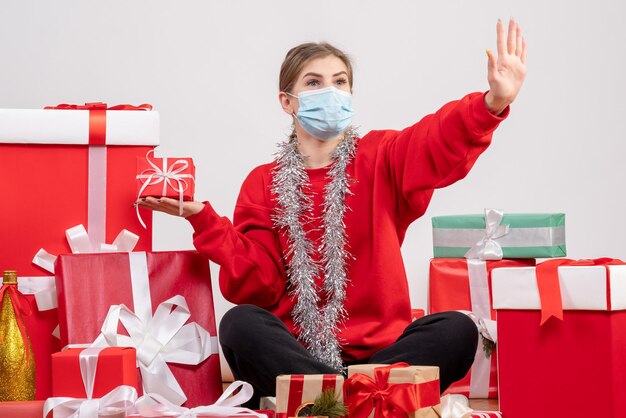 Vue de face jeune femme assise autour de cadeaux de Noël en masque stérile