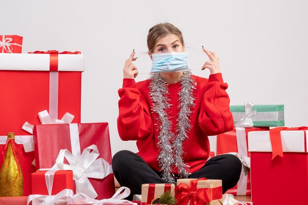 Vue de face jeune femme assise autour de cadeaux de Noël en masque stérile