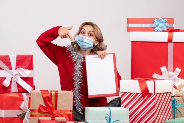 Vue de face jeune femme assise autour de cadeaux de Noël en masque