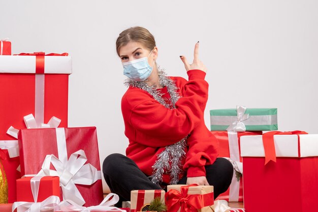 Vue de face jeune femme assise autour de cadeaux de Noël en masque