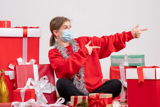 Vue de face jeune femme assise autour de cadeaux de Noël en masque