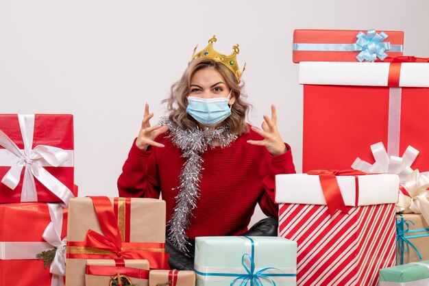 Vue de face jeune femme assise autour de cadeaux de Noël en masque