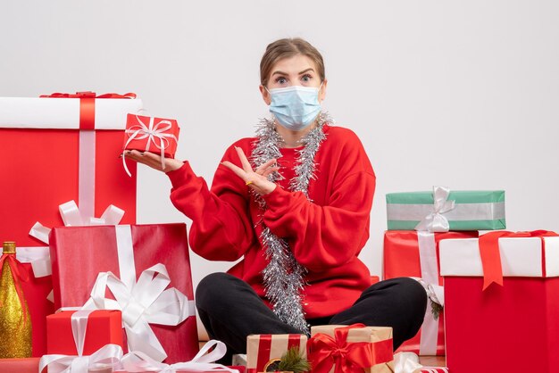 Vue de face jeune femme assise autour de cadeaux de Noël en masque