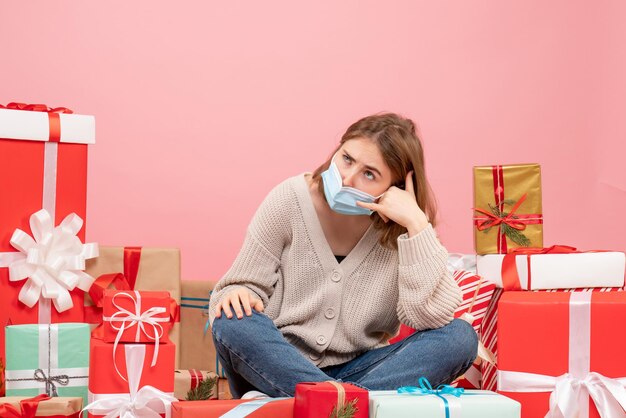 Vue de face jeune femme assise autour de cadeaux de Noël en masque