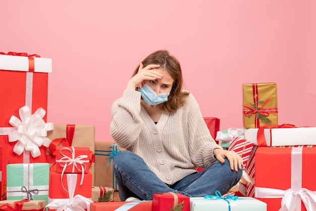 Vue de face jeune femme assise autour de cadeaux de Noël en masque