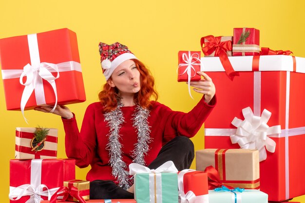 Vue de face de la jeune femme assise autour des cadeaux de Noël sur mur jaune