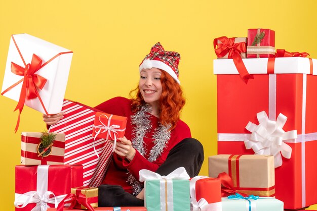 Vue de face de la jeune femme assise autour des cadeaux de Noël sur mur jaune