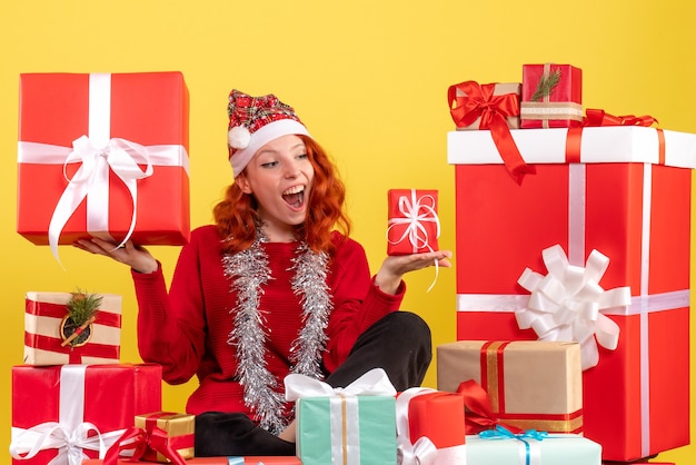 Vue de face de la jeune femme assise autour des cadeaux de Noël sur mur jaune