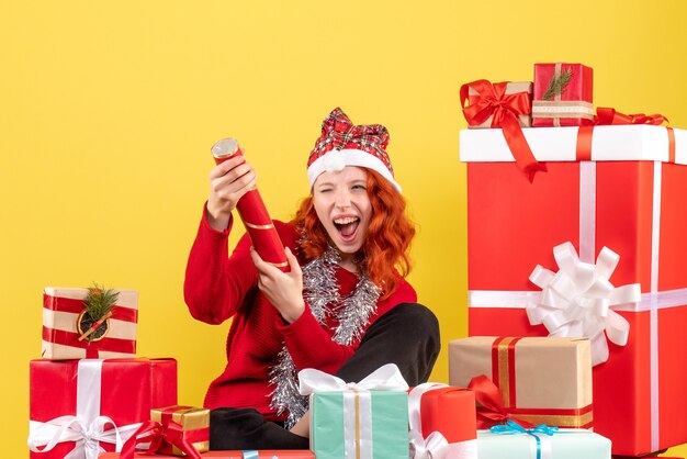 Vue de face de la jeune femme assise autour des cadeaux de Noël sur mur jaune