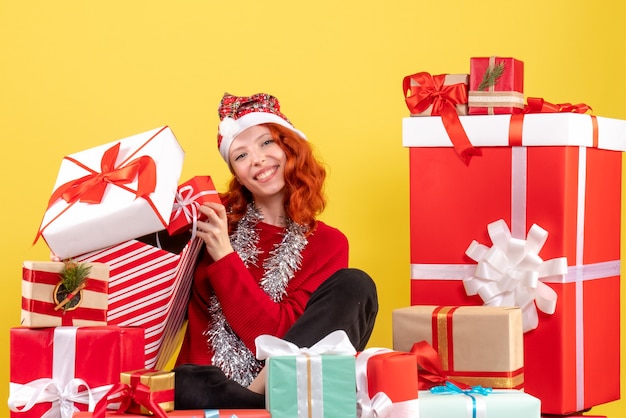 Vue de face de la jeune femme assise autour des cadeaux de Noël sur mur jaune