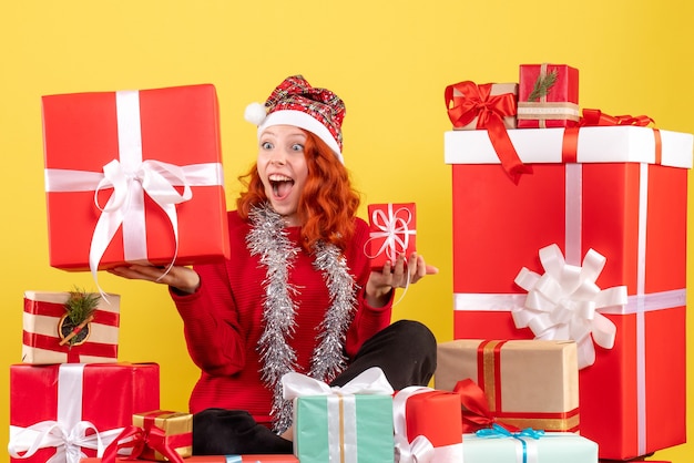 Vue de face de la jeune femme assise autour des cadeaux de Noël sur mur jaune