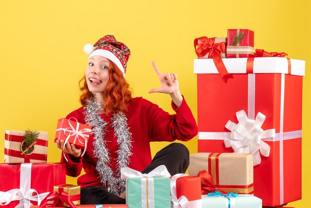 Vue de face de la jeune femme assise autour des cadeaux de Noël sur mur jaune