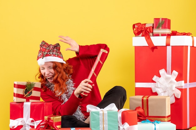 Vue de face de la jeune femme assise autour des cadeaux de Noël sur mur jaune