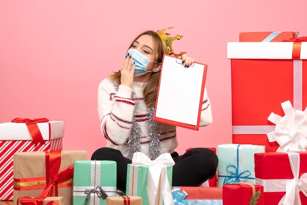 Vue de face jeune femme assise autour de cadeaux de Noël avec note de fichier