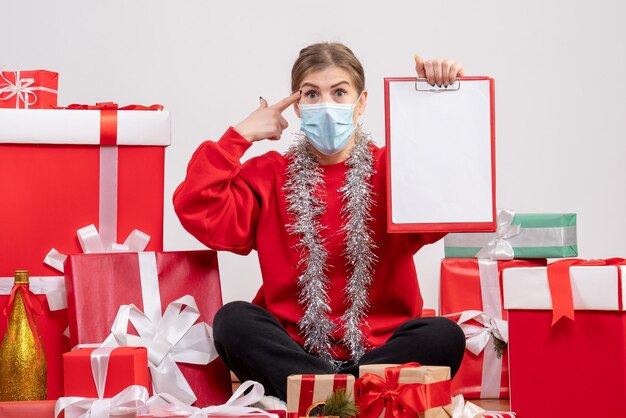 Vue de face jeune femme assise autour de cadeaux de Noël avec note