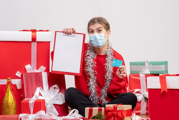 Vue de face jeune femme assise autour de cadeaux avec note et carte bancaire