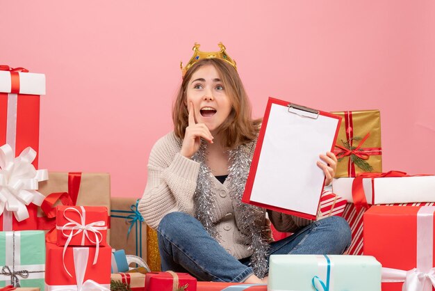 Vue de face jeune femme assise autour de cadeaux avec note dans ses mains