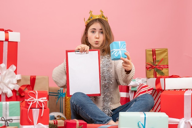 Vue de face jeune femme assise autour de cadeaux avec note dans ses mains