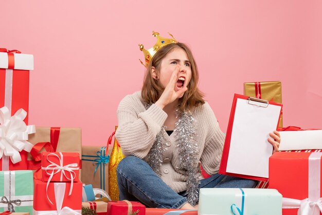 Vue de face jeune femme assise autour de cadeaux avec note dans ses mains