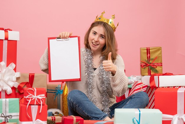 Vue de face jeune femme assise autour de cadeaux avec note dans ses mains