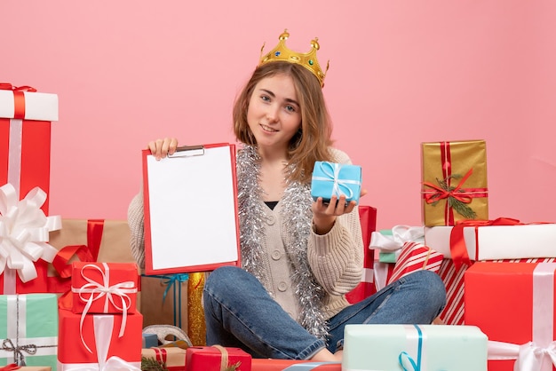 Vue de face jeune femme assise autour de cadeaux avec note dans ses mains