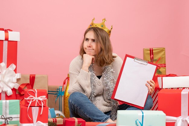 Vue de face jeune femme assise autour de cadeaux avec note dans ses mains