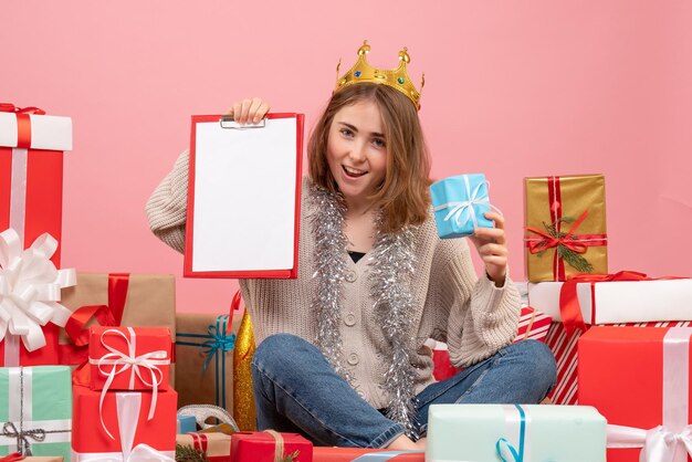 Vue de face jeune femme assise autour de cadeaux avec note dans ses mains