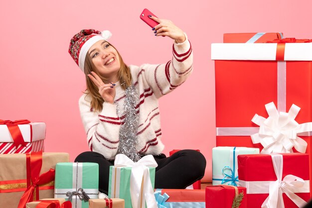 Vue de face jeune femme assise autour de cadeaux prenant selfie