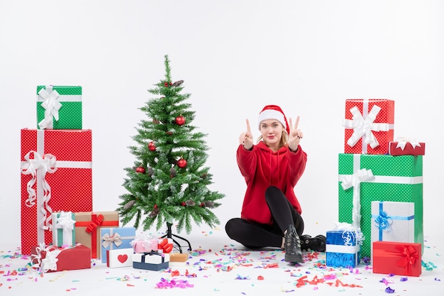 Vue de face de la jeune femme assise autour des cadeaux de vacances comptant sur un mur blanc