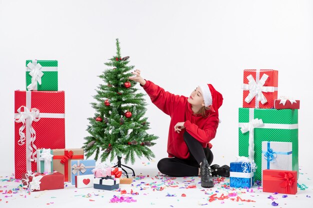 Vue de face de la jeune femme assise autour des cadeaux de vacances sur le mur blanc