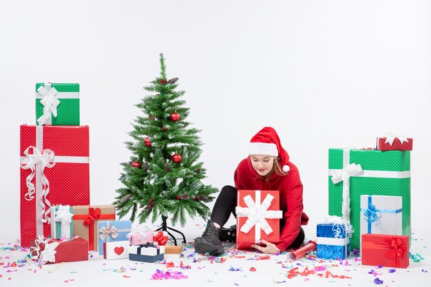 Vue de face de la jeune femme assise autour des cadeaux de vacances sur le mur blanc