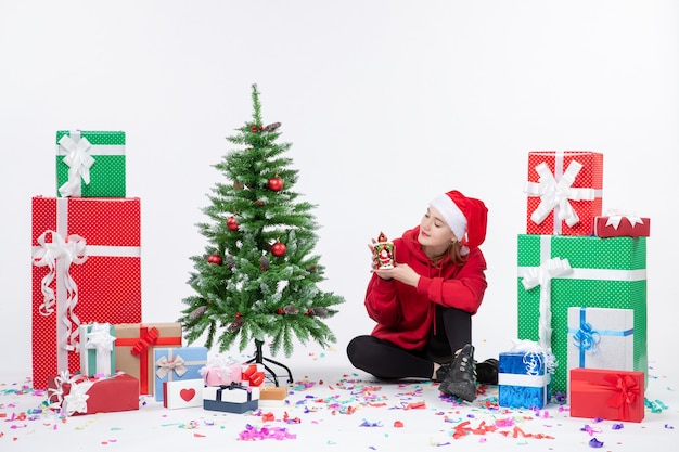 Vue de face de la jeune femme assise autour des cadeaux de vacances sur le mur blanc