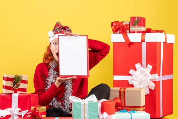 Vue de face de la jeune femme assise autour de différents cadeaux de Noël sur mur jaune