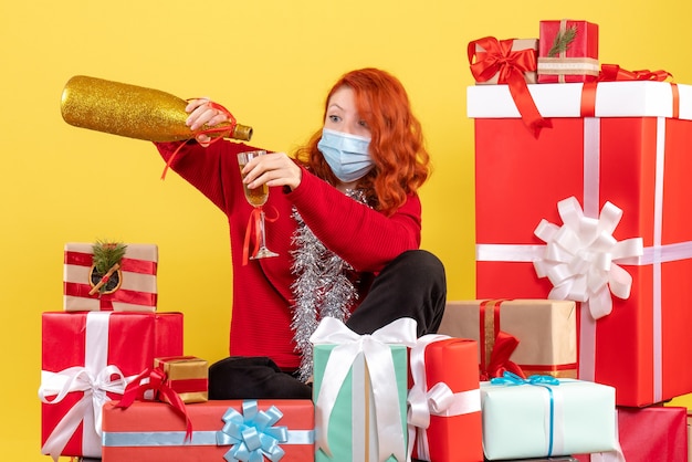 Photo gratuite vue de face de la jeune femme assise autour de noël présente en masque avec champagne sur mur jaune