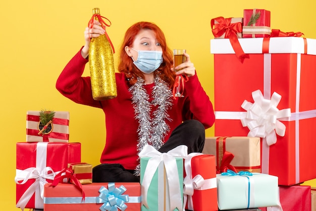 Photo gratuite vue de face de la jeune femme assise autour de noël présente en masque avec champagne sur mur jaune