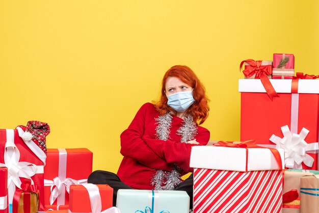 Vue de face jeune femme assise autour de Noël présente avec masque sur jaune nouvel an émotion covid- couleur virus