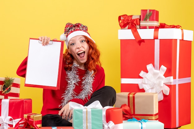 Vue de face de la jeune femme assise autour de Noël présente avec note de fichier sur mur jaune